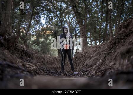 Female wearing a skeleton costume and skull makeup on her face in the middle of a creepy forest Stock Photo
