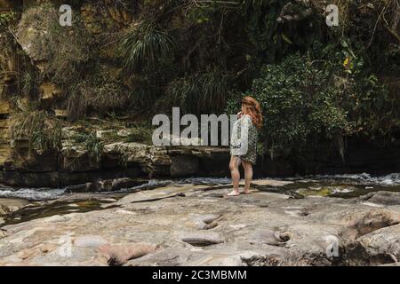 CURITI, COLOMBIA - Apr 13, 2019: Wide shot of a young woman standing in the river looking thoughtful and wondering about climate change Stock Photo