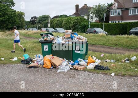 WIMBLEDON LONDON, UK. 21 June 2020. A jogger run past  bins  overflowing with rubbish including empty pizza boxes, beer bottles, cans  and plastic bags on Wimbledon Common, after the government eased lockdown restrictions and allowed people to congregate in groups of up to six outdoors. Credit: amer ghazzal/Alamy Live News Stock Photo