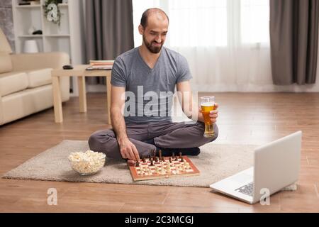 Young man smiling while playing chess with friends on video call. Stock Photo