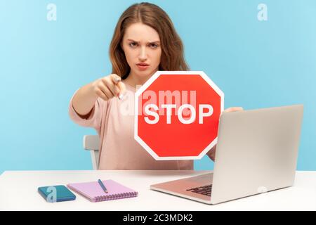 Angry woman boss, office employee at workplace, holding stop symbol and pointing to camera, showing red traffic sign, negative prohibition concept. in Stock Photo