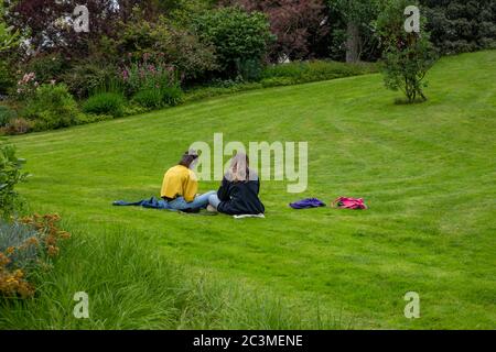 two young women sitting on grass, rear view, girl frends together, students