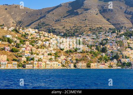 Late afternoon sun over neo-classical mansions of Gialos port and the old hillside Horio, Symi Island, Dodecanese, Greece Stock Photo