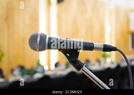 Close up to microphone beside the podium with blur long black table dinner time in tungsten warm light. Stock Photo