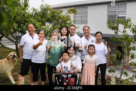 (200621) -- ANKANG, June 21, 2020 (Xinhua) -- Li Zengyi (1st L) and his family pose for a photo in Wenhua Village in Hanbin District of Ankang City, northwest China's Shaanxi Province, June 19, 2020. In 1997, in order to shake off poverty, Li Zengyi, a villager in Wenhua Village of Ankang City, moved his family, including his seven-year-old disabled daughter, to a makeshift house on a mountain to cultivate peaches. Li Wei, the elder son of Li Zengyi, went out to work in south China's Guangdong Province after graduation from middle school to support the family. Li Peng, the younger son, con Stock Photo