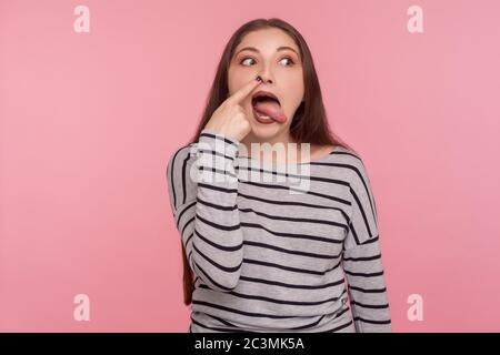 Bad habit. Portrait of funny woman in striped sweatshirt drilling nose with humorous stupid expression, making silly grimace, sticking out tongue. ind Stock Photo