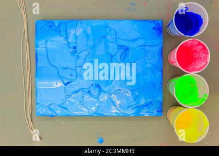 Artist Canvas covered with Psychedelic looking Blue paint and paint in plastic cups to the side Stock Photo