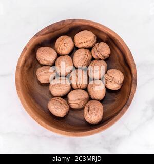 Walnut in wooden bowl on light marble background. Flatlay, top view. Wooden plate with walnuts. Space for text. Organic food, natural foods Stock Photo