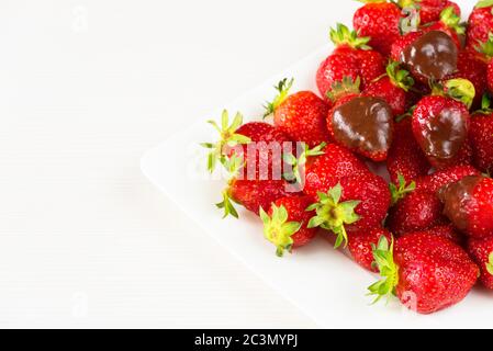 Strawberries dipped in delicious chocolate in white dish isolated on white background. Close up view. Stock Photo