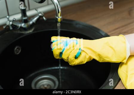 Sponge for washing dishes in hand. Blue sponge washing liquid soap on dirty sink dishes and kitchen ware. Stock Photo
