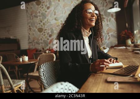 Smiling woman having a video call on her laptop at coffee shop. Business professional sitting at cafe table having a video conference. Stock Photo