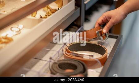 Female hand choosing the roll leather belt in the drawer shelf for the decision to buy, Fashion and shopping concept. Stock Photo