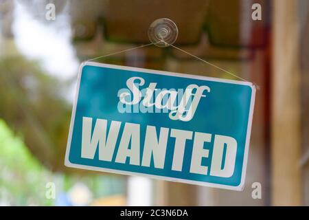 Close-up on a blue open sign in the window of a shop displaying the message: Staff wanted. Stock Photo