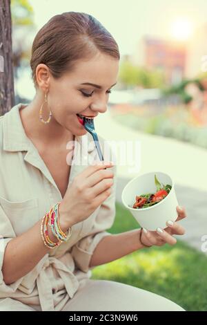 Young cheerful latina woman eating salad in park Stock Photo