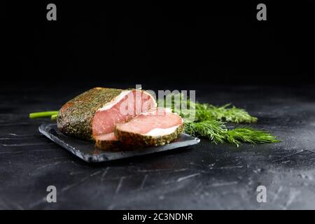 Dried pork, polendwitz, jerky tenderloin, fresh green dill, slate cutting board on black background. Cured pork meat. Polenitsa is a dry-cured filet. Stock Photo