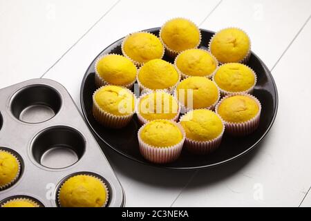 Cupcakes on black plate, baking tray on white wooden table. Pumpkin muffins. Homemade bakery Stock Photo