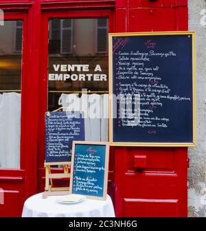 A menu stands on a table and on the wall  displaying a selection of food that the restaurant serves in France Stock Photo