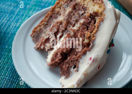A piece of chocolate sponge cake with cream on a white plate close up decorated with multicolored topping Stock Photo