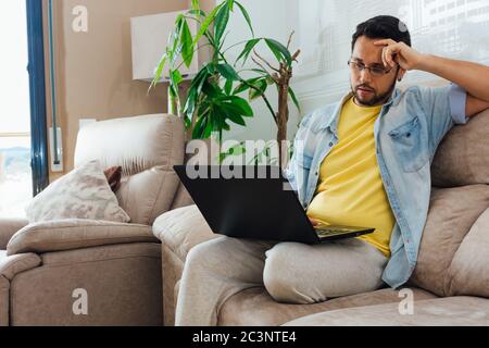 Photo of a handsome Hispanic man sitting on a sofa and using a laptop Stock Photo