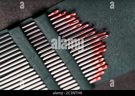 Sewing needles of different sizes in a set of red on a black background. Stock Photo