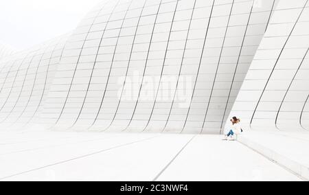 Baku, Azerbaijan - January 01, 2018: Beautiful woman in white sits on the white wall of Heydar Aliev Center in Baku, Azerbaijan Stock Photo