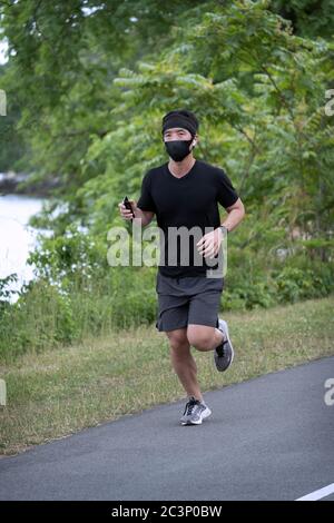 An Asian American man, likely Korean, runs on a path wearing a surgical mask and using Air Pods. In Bayside, Queens, NYC. Stock Photo