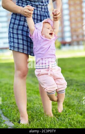 Mother teaching her baby to take the first steps barefoot on the grass. Stock Photo