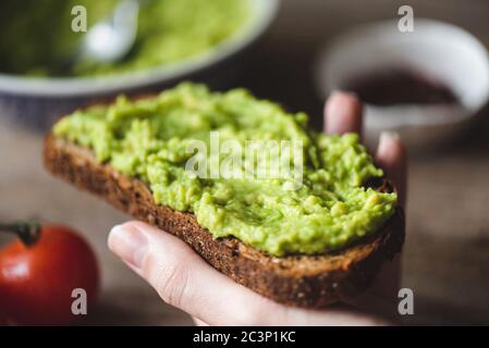 Toast with mashed avocado. Hand holding avocado rye bread toast. Healthy vegan vegetarian food Stock Photo