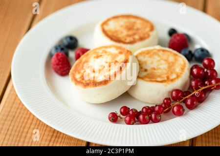 Russian Syrniki, Cottage cheese fritters or pancakes served with red currant berries, blueberries and raspberries Stock Photo