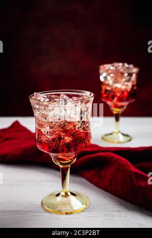 Two beautiful refreshing sparkling cocktails with ice, white wooden table, dark background with red tint, red napkin Stock Photo