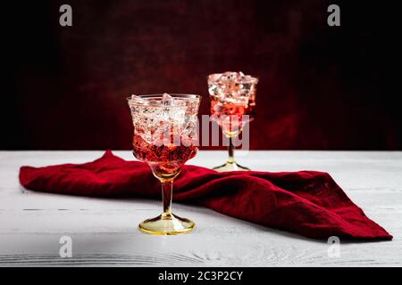 Two beautiful refreshing sparkling cocktails with ice, white wooden table, dark background with red tint, red napkin Stock Photo