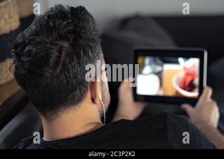 man hand holding using digital tablet watching online cooking master class using headphones. learning cooking remotely Stock Photo