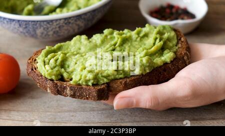 Rye bread toast with mashed avocado. Healthy vegan vegetarian breakfast or snack food. Avocado toast in hand Stock Photo
