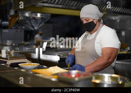 cooking, profession and people concept - woman in age chef wearing protective black mask on her face while working in restaurant kitchen Stock Photo