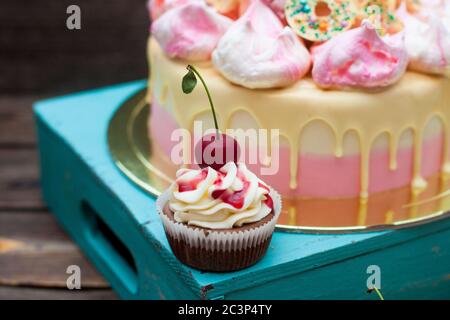 Chocolate cupcake with berry sauce, whipped cream and fresh cherry on top. Pink cake on the background. Stock Photo
