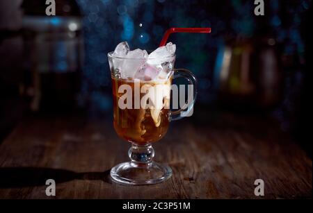 Ice coffee in a latte glass with cream poured over, ice cubes and beans on a old rustic wooden table. on a black background with copy space. Stock Photo