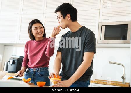 Lovely youg asian couple cooking breakfast together in the kitchen, squeezing oranges for juice Stock Photo