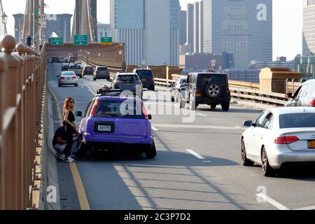 People with a disabled car on a busy Brooklyn Bridge roadway in New York. Stock Photo