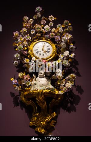 Closeup shot of a golden wall clock with flowers and a Buddha figure Stock Photo