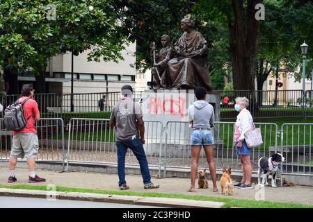 Raleigh, NC, United States, June 20, 2020 - People gather in front of the defaced statue honoring Women of the Confederacy as word spreads that it is being taken down. The decision came the morning after Juneteenth protesters, sparked by the police killing of George Floyd, succeed in pulling two figures off of the neighboring 70-foot tall Confederate Memorial column. The morning of the 20th the Governor of NC ordered it and two other Confederate monuments to be removed from the grounds of the Old Capitol Building. Stock Photo