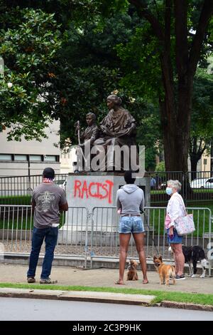 Raleigh, NC, United States, June 20, 2020 - People gather in front of the defaced statue honoring Women of the Confederacy as word spreads that it is being taken down. The decision came the morning after Juneteenth protesters, sparked by the police killing of George Floyd, succeed in pulling two figures off of the neighboring 70-foot tall Confederate Memorial column. The morning of the 20th the Governor of NC ordered it and two other Confederate monuments to be removed from the grounds of the Old Capitol Building. Stock Photo