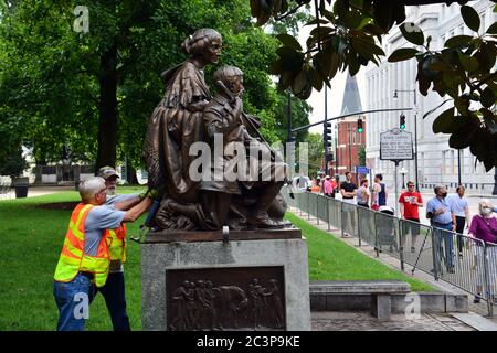 Raleigh, NC, United States, June 20, 2020 - As a crowd watches workers separate the statue honoring Women of the Confederacy from its base for removal. The decision came the morning after Juneteenth protesters, sparked by the police killing of George Floyd, succeed in pulling two figures off of the neighboring 70-foot tall Confederate Memorial column. The morning of the 20th the Governor of NC ordered it and two other Confederate monuments to be removed from the grounds of the Old Capitol Building. Stock Photo