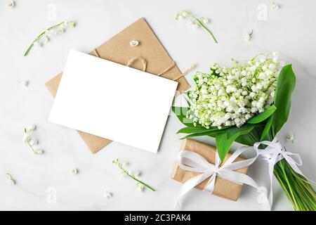 blank greeting card with lily of the valley flowers bouquet and gift box on white background. mock up. top view. flat lay. wedding invitation Stock Photo
