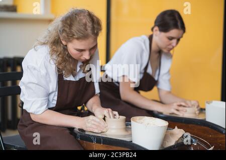 Two female ceramic artists in apron using clay material working in potter studio. Evening freelance distance learning. Adult hobby adventure. Winter Stock Photo
