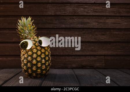 Cool pineapple with sunglasses on and dark wooden background Stock Photo