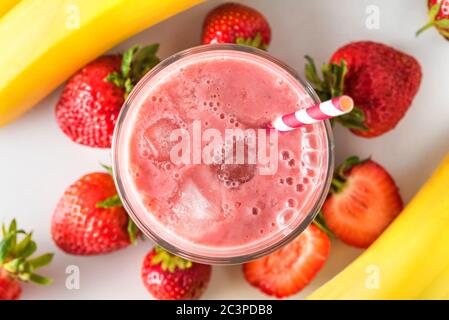 Strawberry and banana smoothie or milkshake in a glass with ice cubes and straw with fresh fruits. top view. refreshing summer drink Stock Photo