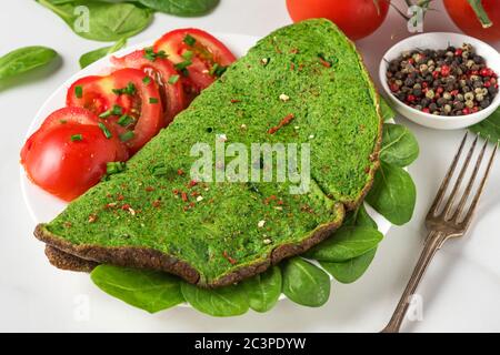 Healthy breakfast. Green spinach omelet with tomatoes and spices with fork on white marble table. keto diet food. close up Stock Photo