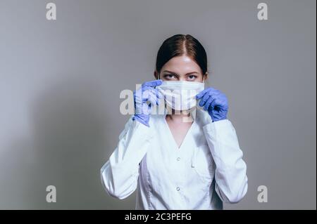 Woman doctor in a white coat wears a protective mask for work Stock Photo