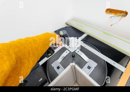 Overhead view of male carpenter worker holding in cordless hand drill installation of rotating baskets - kitchen reconstruction renovation an repairing Stock Photo