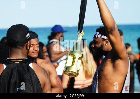 MIAMI - MARCH 16, 2019: A young man dangles a golden bottle of liquor at a gathering of college students celebrating spring break on South Beach. Stock Photo